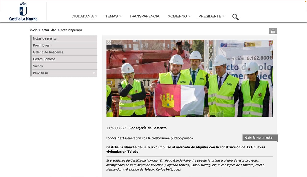 Un grupo de personas con cascos y chalecos de construcción sostienen con orgullo una bandera en un evento en la obra de Toledo, en el que aparece una pancarta sobre vivienda. Easier Gestión juega un papel clave en la ejecución sin problemas del proyecto.