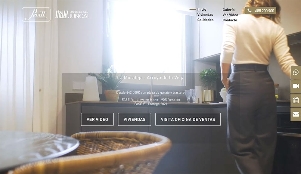 Persona de pie junto a la encimera de una cocina vista desde atrás con una pantalla de ordenador que muestra en primer plano un sitio web inmobiliario para facilitar la gestión.